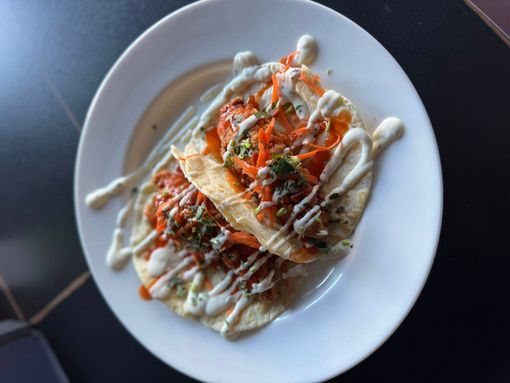 Two tostadas with carrots, herbs, and drizzle on a white plate.