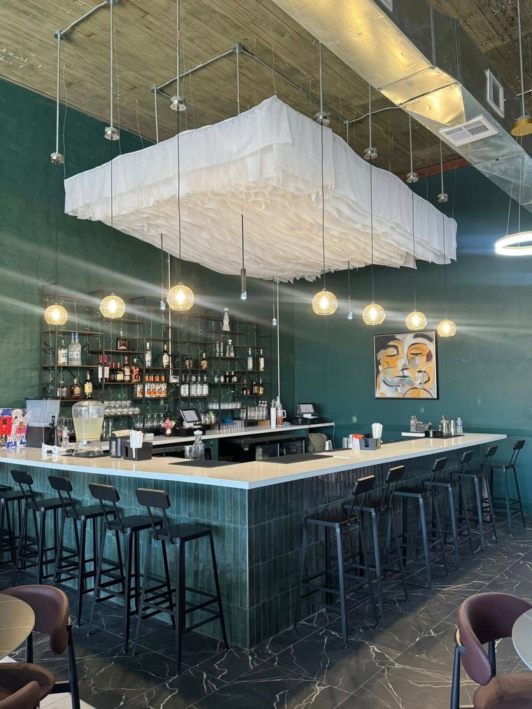 Bar interior with green tiled walls, a long bar, and pendant lights.