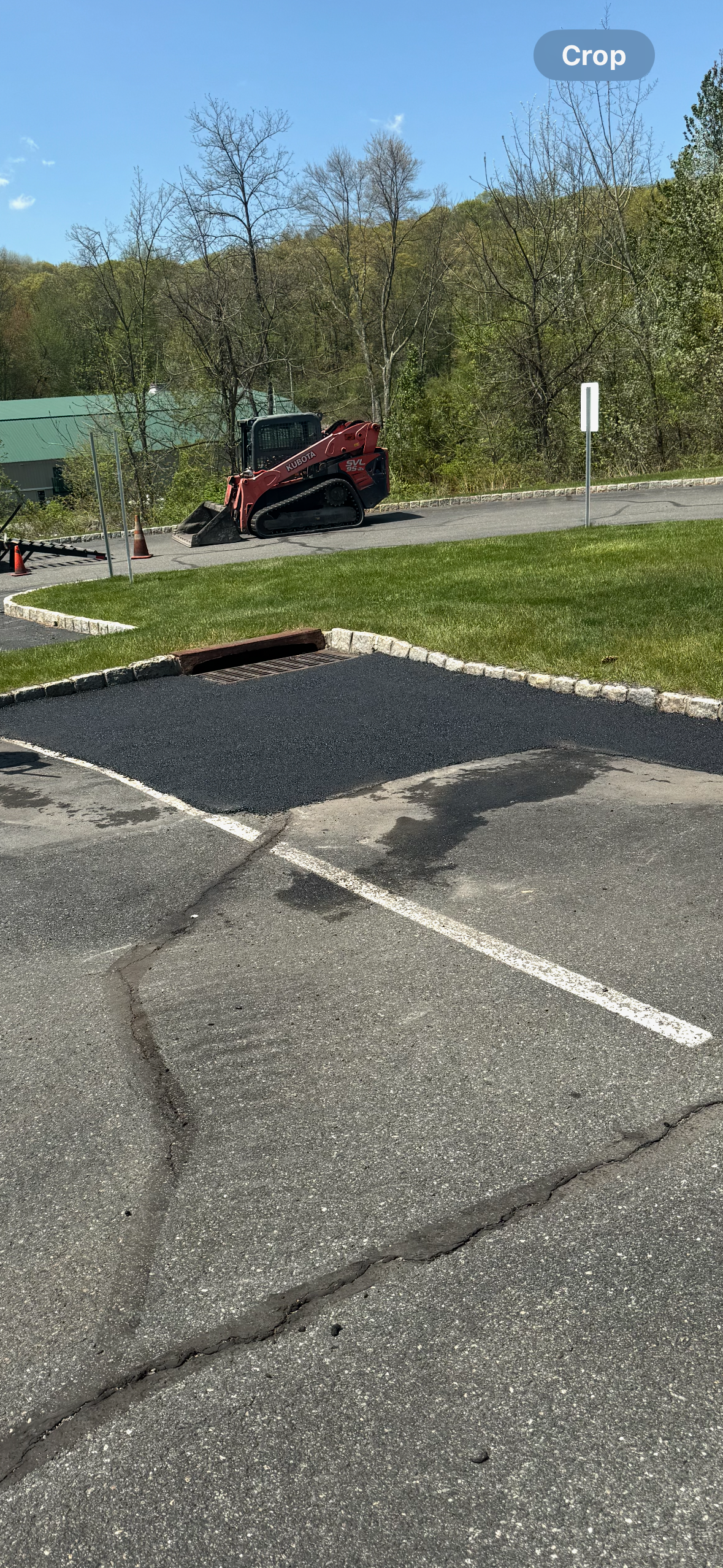 Road workers in orange high-visibility gear spread fresh asphalt on a road surface using rakes.