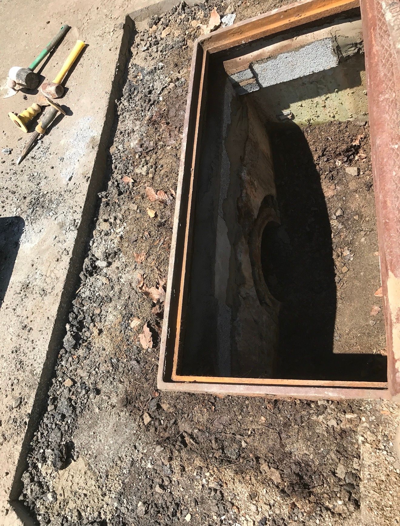 A rectangular concrete utility access pit in the ground next to a set of construction tools.