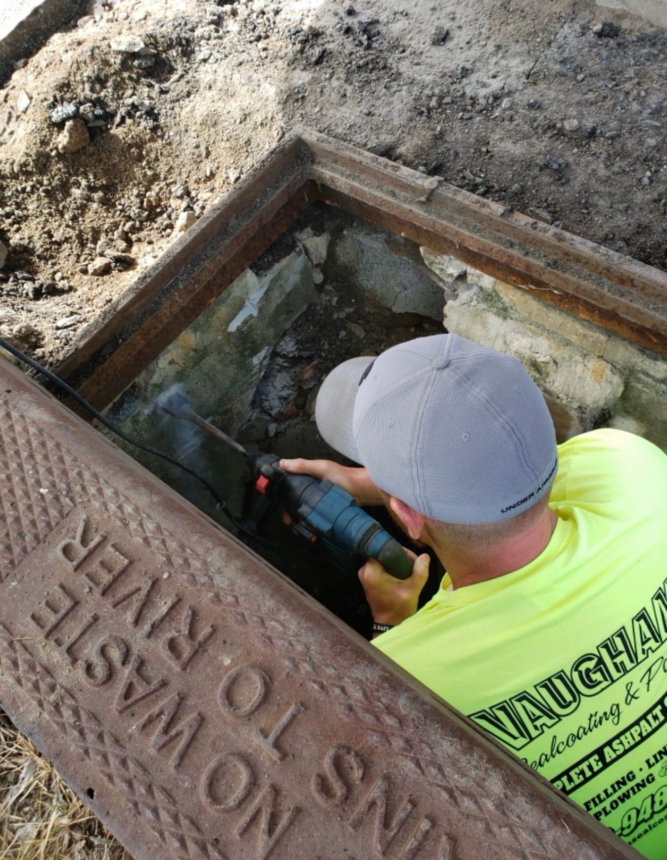 A worker in a bright yellow shirt uses a power tool inside an open storm drain marked 