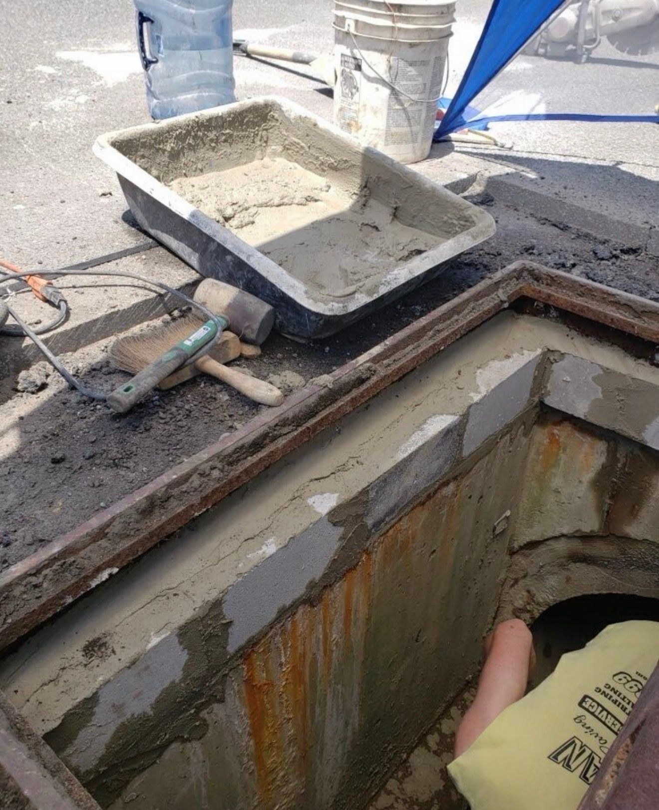 A person in a light yellow shirt works on a concrete drainage structure with mortar, tools, and buckets nearby.