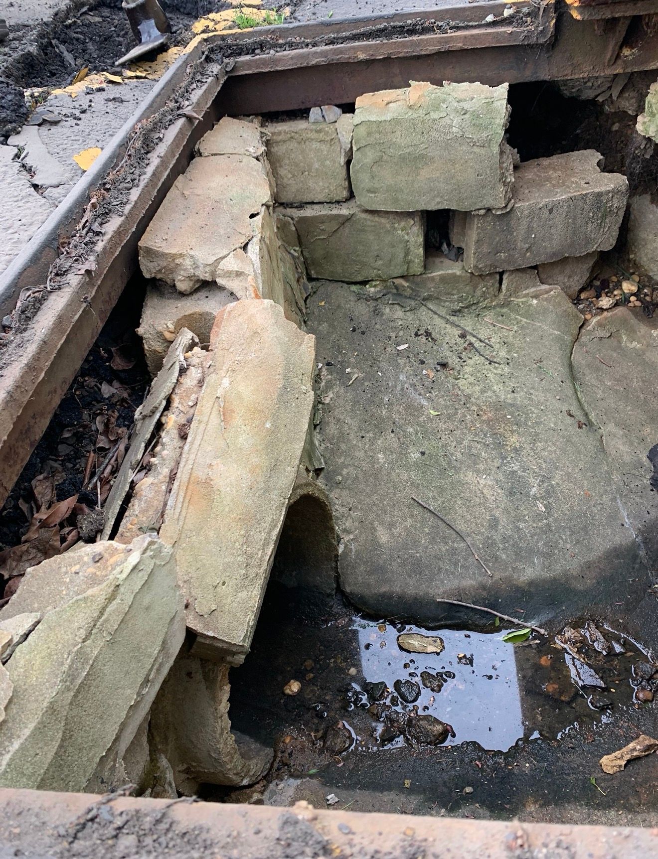 A damaged concrete drainage catch basin with loose cinder blocks and standing water.