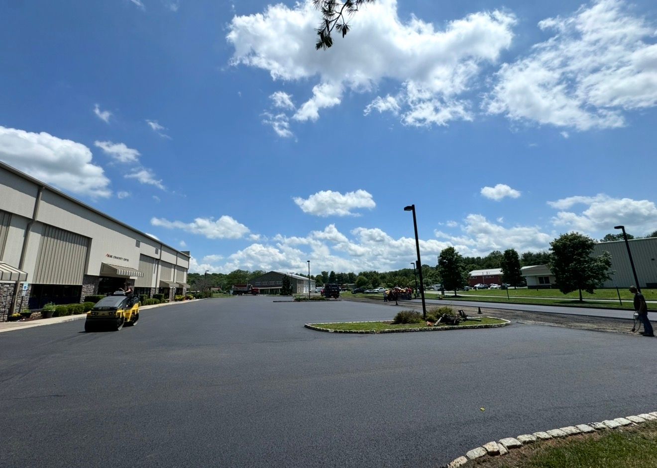 A large, paved commercial parking lot under a bright blue sky with scattered clouds, with a building on the left.