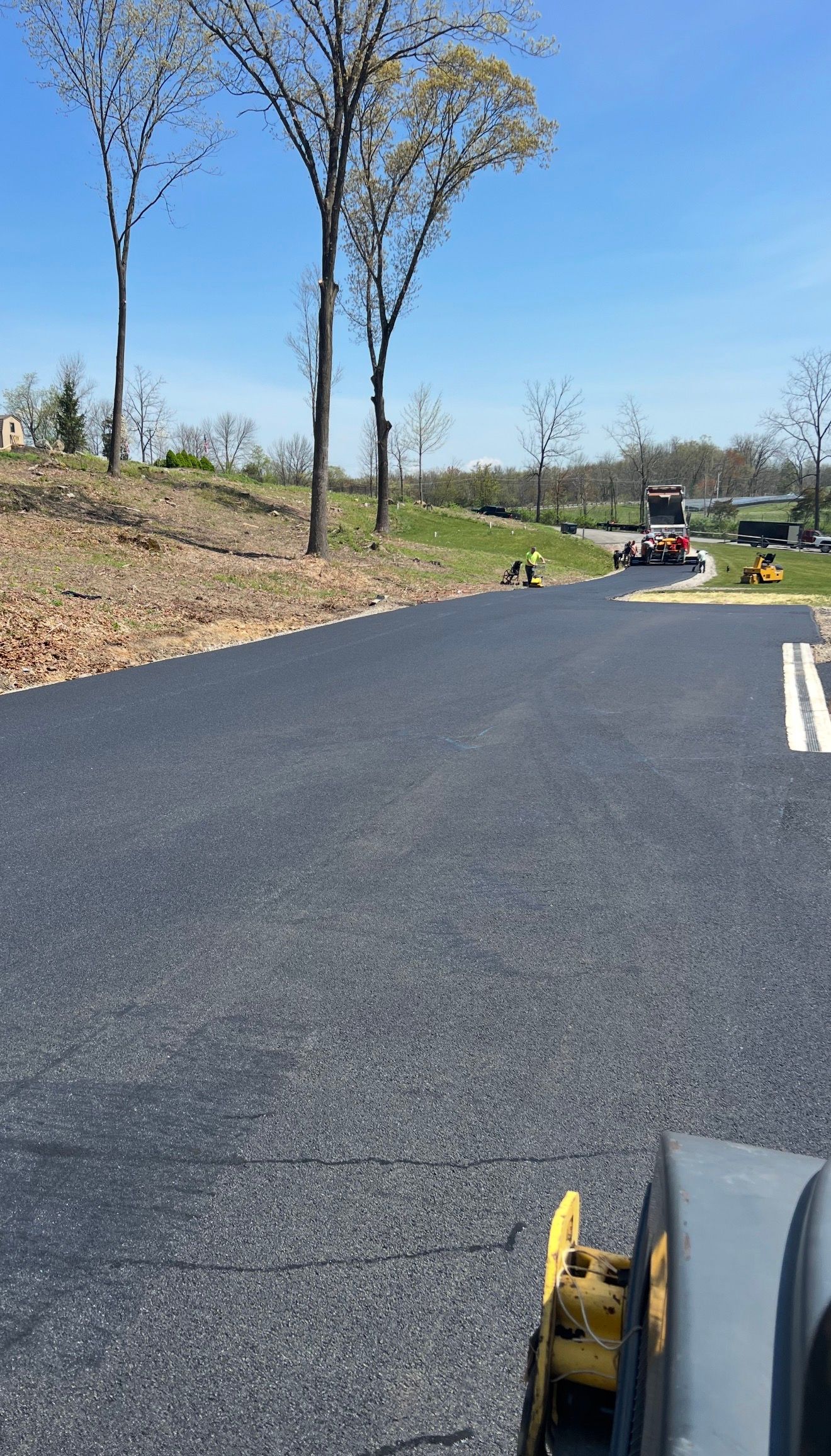 Freshly paved asphalt driveway leading uphill with construction machinery in the distance on a sunny day.