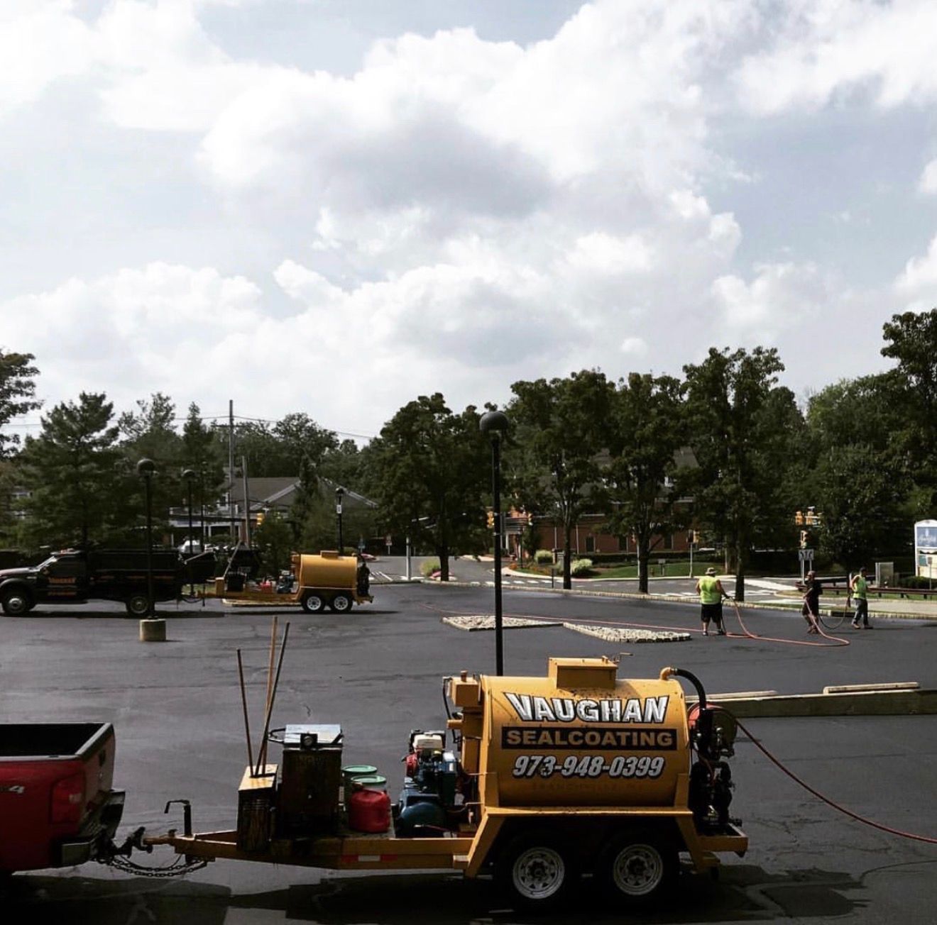 A Vaughan Sealcoating trailer in a parking lot, with crew members applying sealant to the asphalt surface nearby.