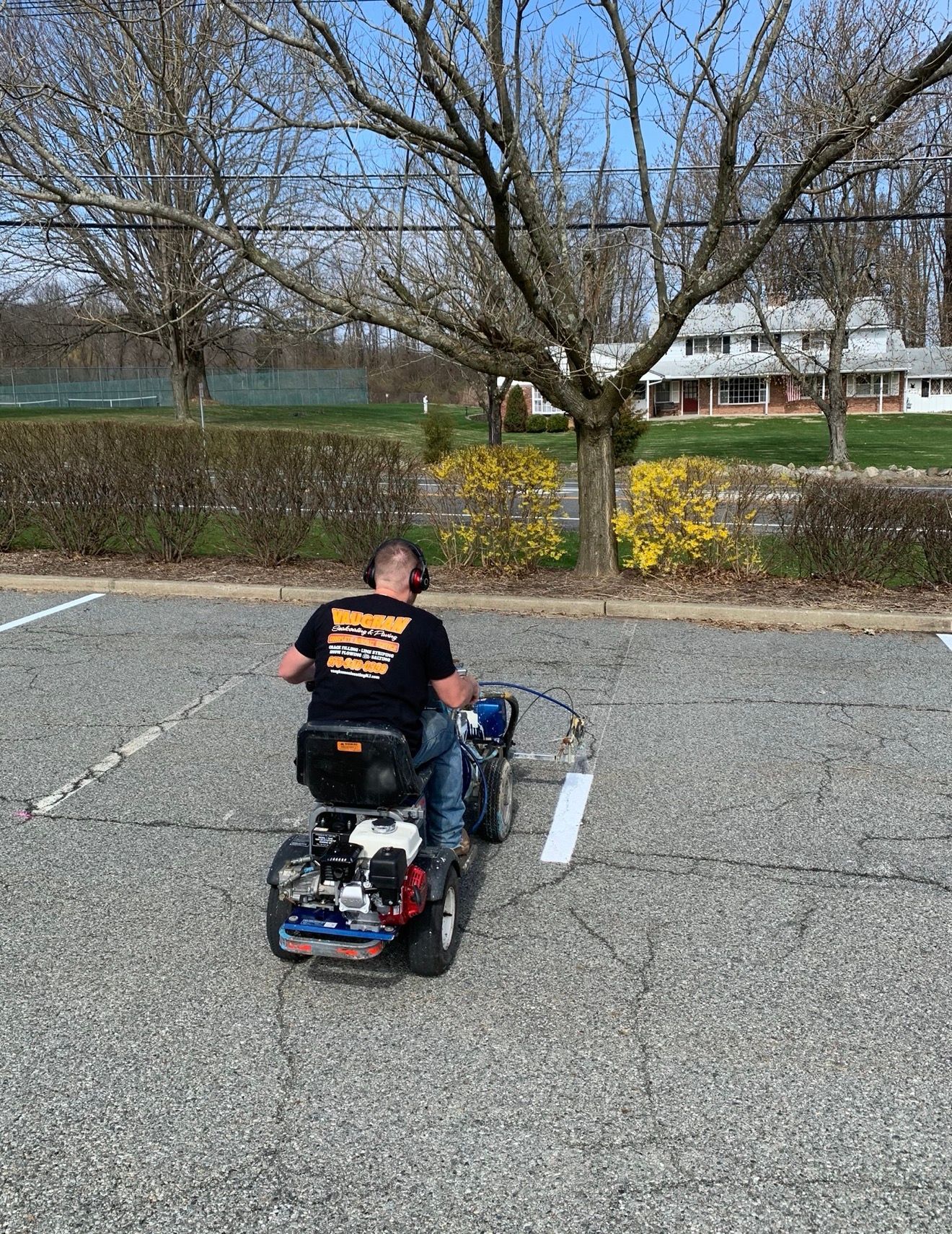 A person operating a line-striping machine to paint a white parking space line in a gravel parking lot.