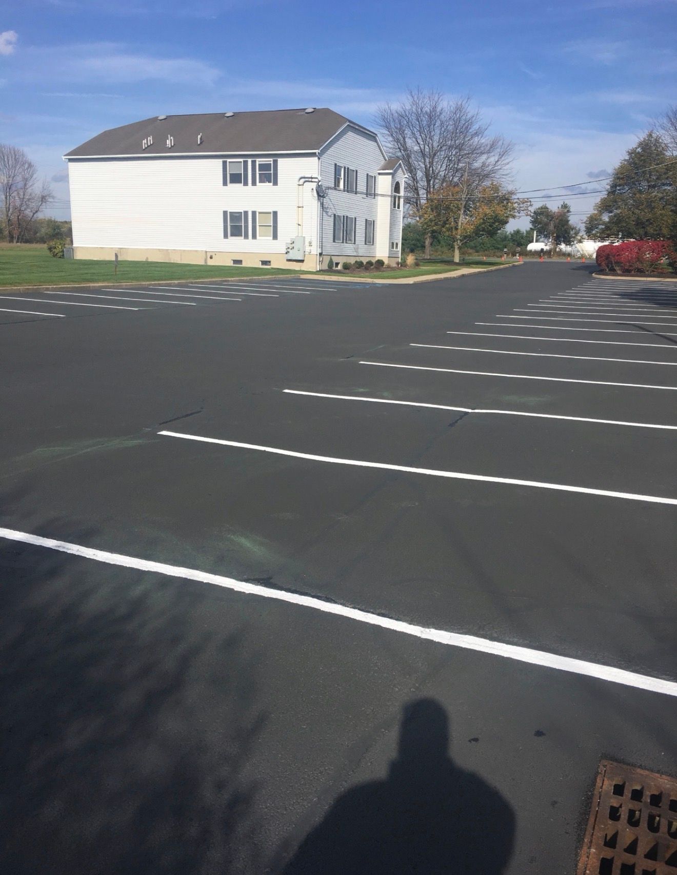An empty parking lot with dashed white lane markings in front of a white two-story residential building on a sunny day.