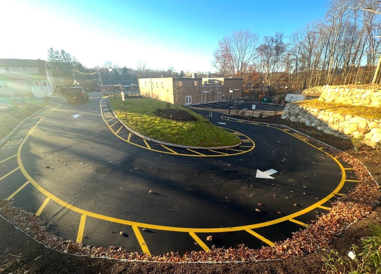 A semi-circular paved driveway loops around a green island, with yellow parking markings and a building in the background.