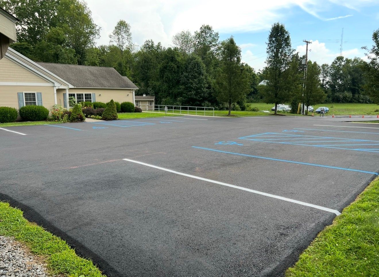 A freshly paved parking lot with white and blue painted parking space lines in front of a tan building and green trees.