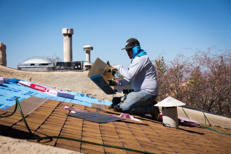 A man is kneeling on a roof working on a roof.