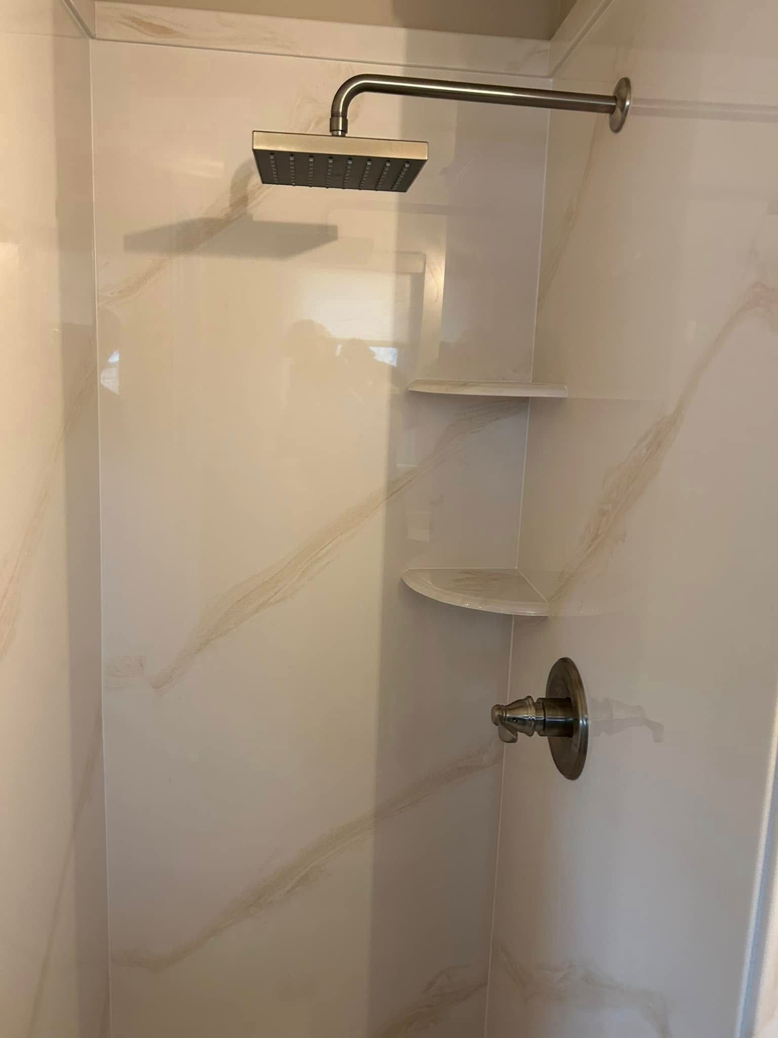 Shower stall with white walls, shelves, and chrome fixtures.