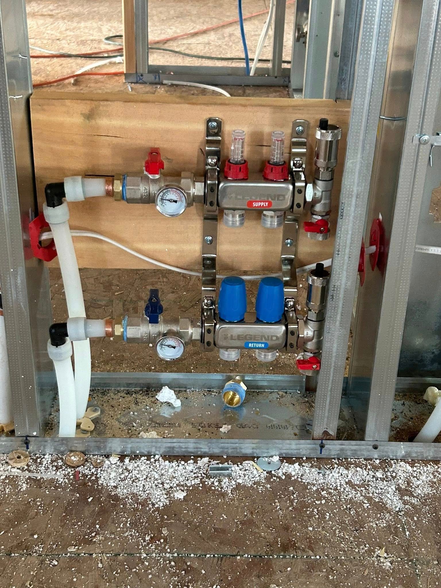 Plumbing manifold system installed on a wooden panel, within a metal frame construction. Includes valves and gauges.