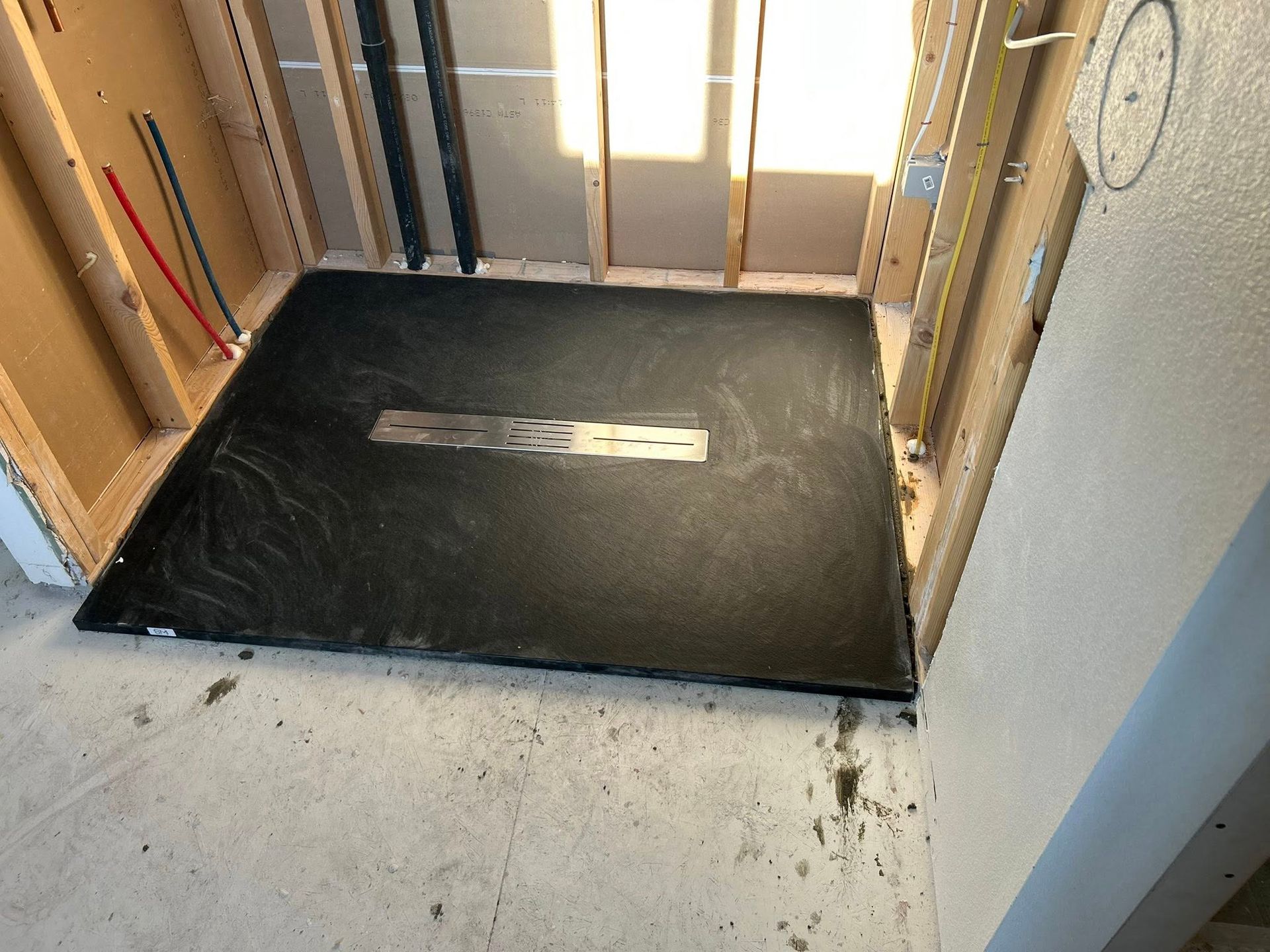 Framed shower area with a dark, textured floor and drain installed. Construction in progress.