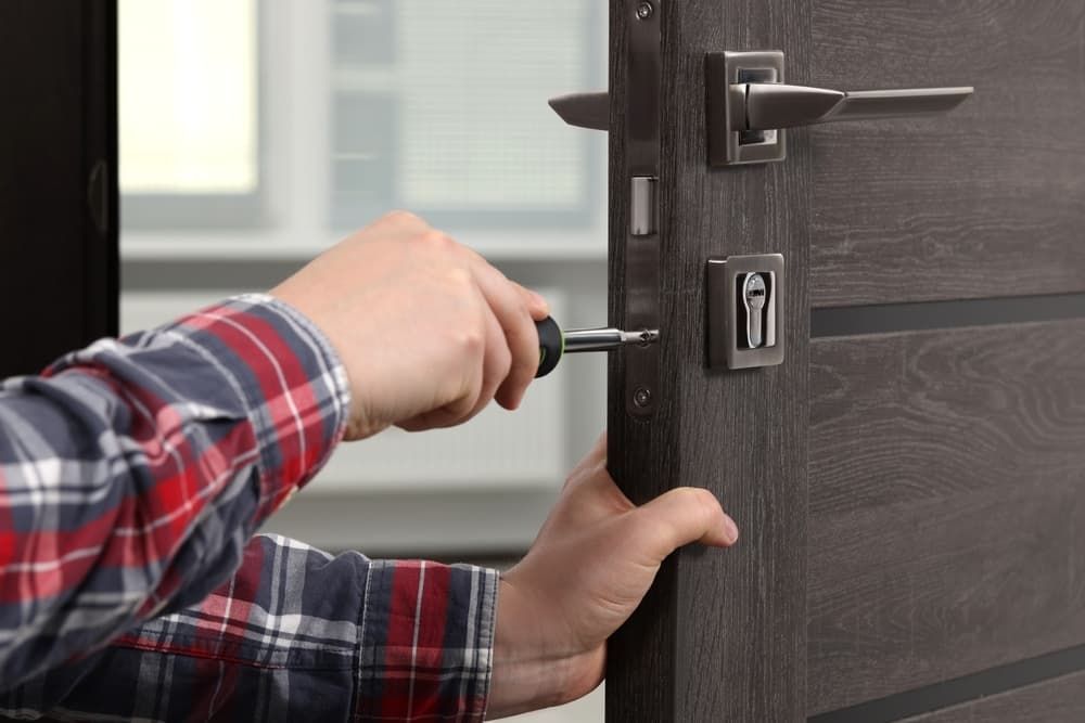 A Man Is Fixing a Door with A Screwdriver — East Coast Locksmiths in Port Wauchope, NSW
