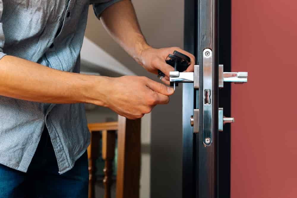 A Man Is Fixing a Door Lock with A Tool — East Coast Locksmiths in Lake Cathie, NSW