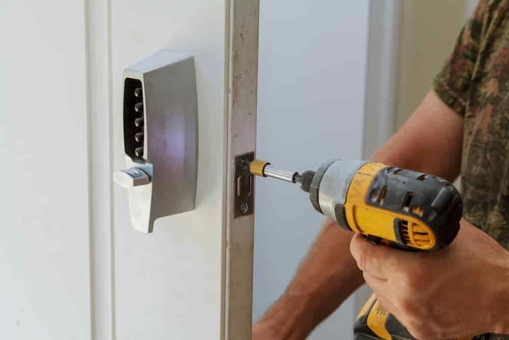A Man Is Using a Drill to Install a Door Lock — East Coast Locksmiths in Lake Cathie, NSW
