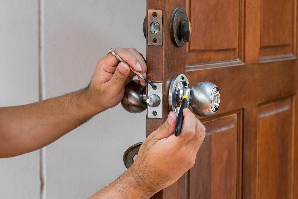A Man Is Fixing a Door Knob with A Screwdriver — East Coast Locksmiths in Port Macquarie, NSW