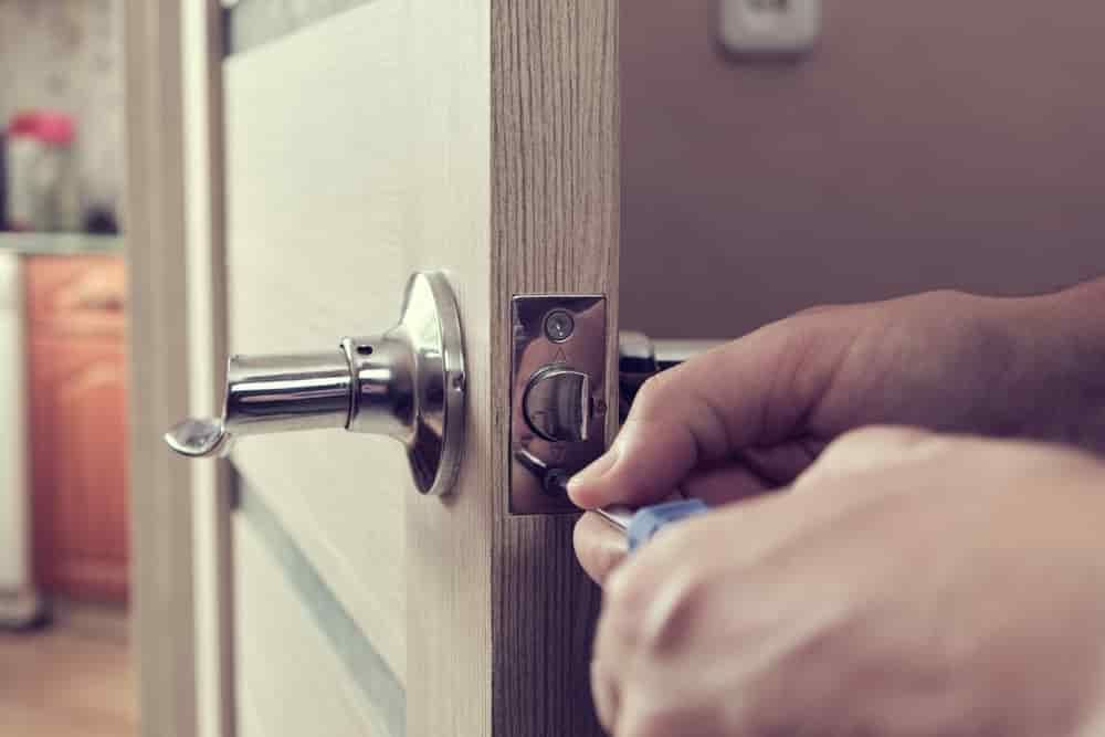 A Person Is Fixing a Door Handle with A Screwdriver — East Coast Locksmiths in Lake Cathie, NSW