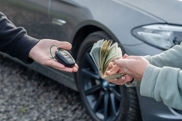 Deal of selling a car concept. Hand with the car keys, other hand gives money with a car behind.