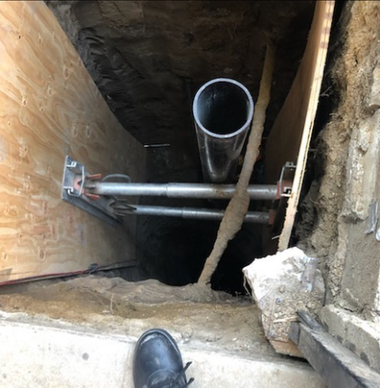 Down a dark crawlspace, a pipe and metal support braces are visible beside a boot at the edge.