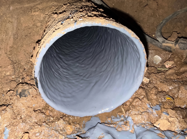 Large white pipe opening in a dirt and rocky excavation, viewed from the end