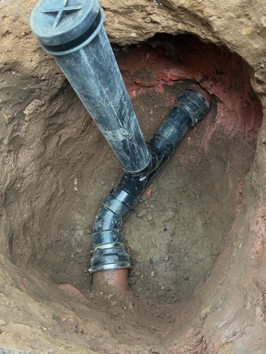 Open trench with black underground pipes connected to a vertical vent pipe.