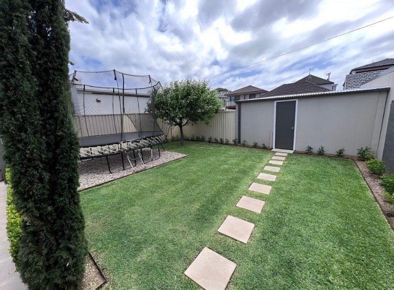 A Lush Green Backyard With a Stone Walkway Leading to a Shed — Superior Turf in Shellharbour, NSW
