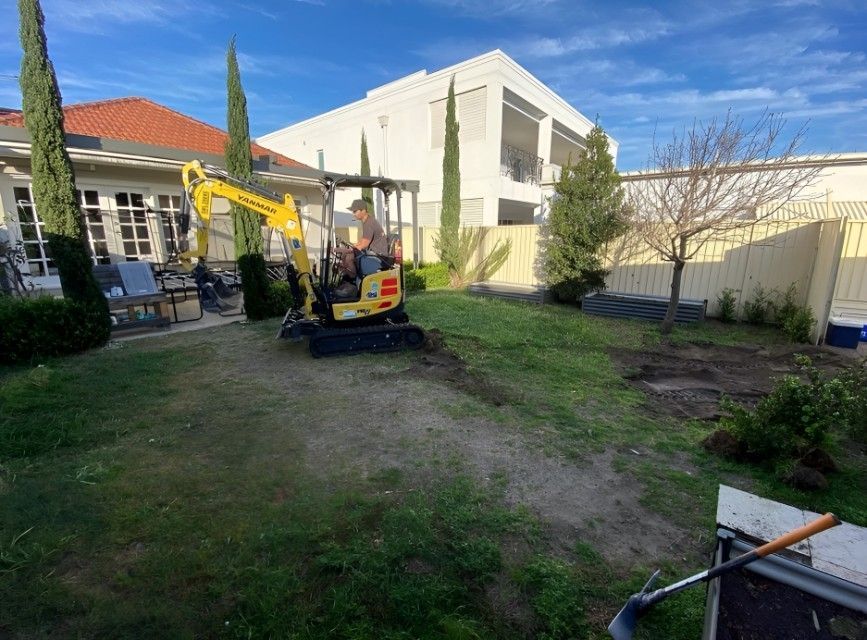 A Man is Driving a Small Excavator in a Backyard — Superior Turf In Shoalhaven, NSW