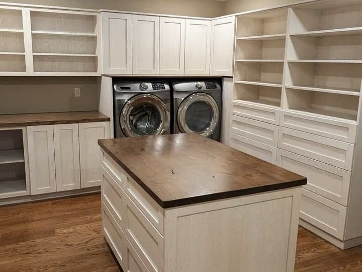 Luxury master closet and laundry room suit with custom white cabinetry, open shelving, and a large wood-top folding island in Mid-Missouri home.  