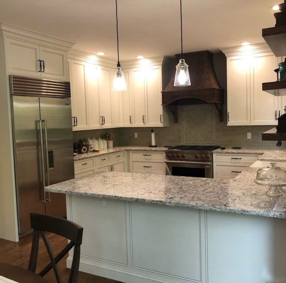 Wrap- around custom white kitchen cabinets with granite countertops, integrated stainless steel refrigerator, and dark wood range hood in a Mid-Missouri home. 