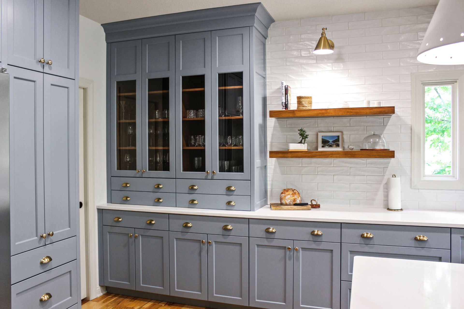 Custom slate blue dining hutch with glass-front cabinets and matching floating wood shelves in a Columbia MO home. 