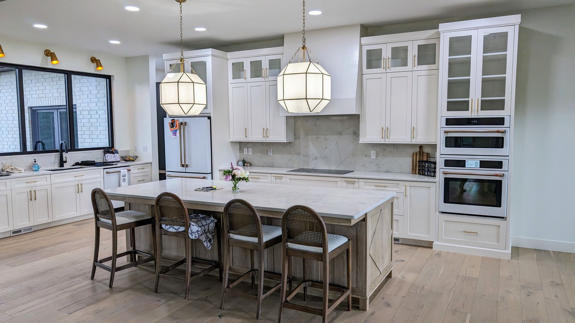 Luxury contemporary white kitchen with glass- front upper cabinets, a massive waterfall island, and geometric pendant lighting in a Mid- Missouri home. Custom cabinets Columbia Missouri 
