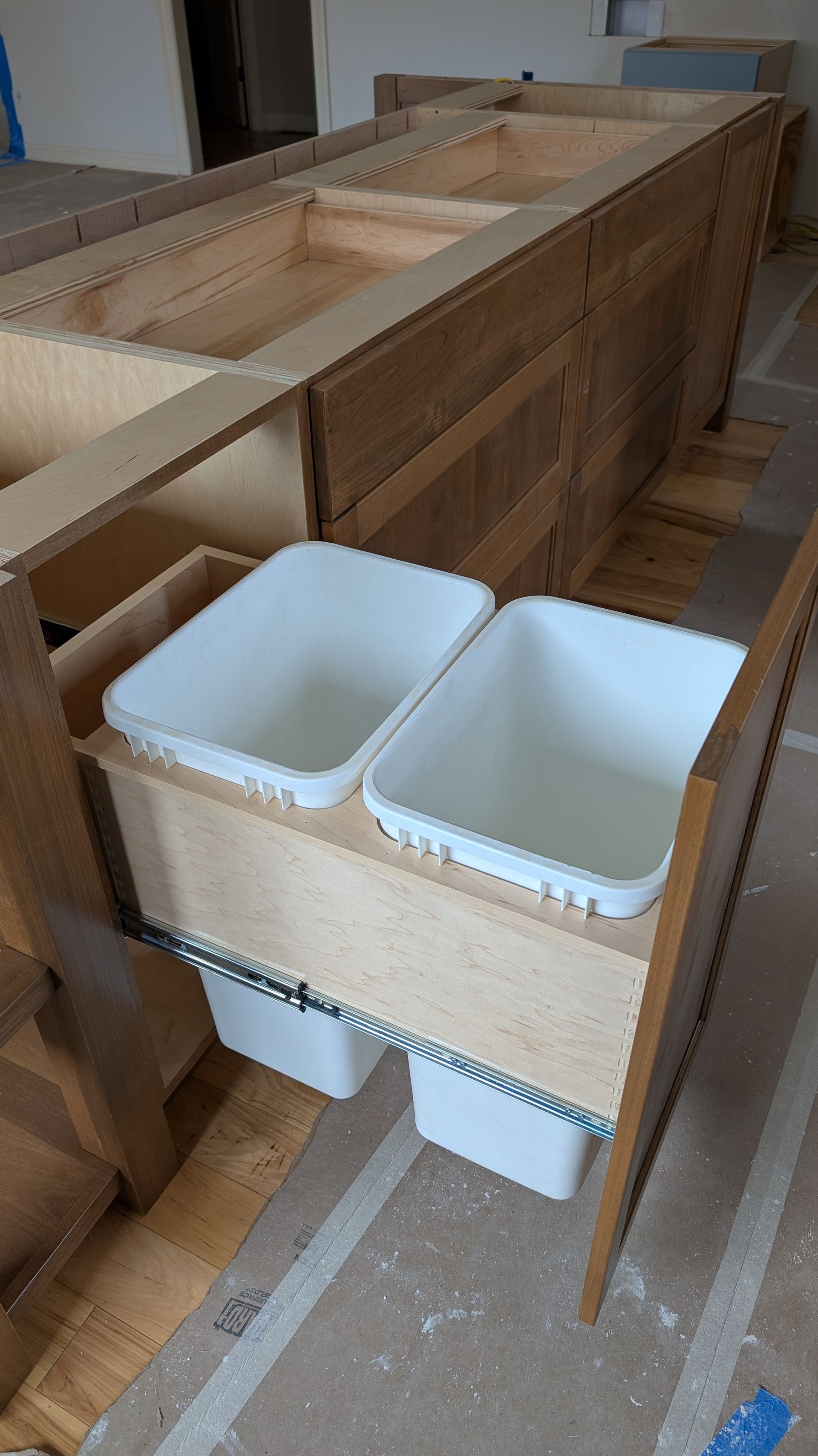 Two white trash cans are pulled out of a wooden cabinet. Custom kitchen cabinets with storage solutions in Mid- Missouri 