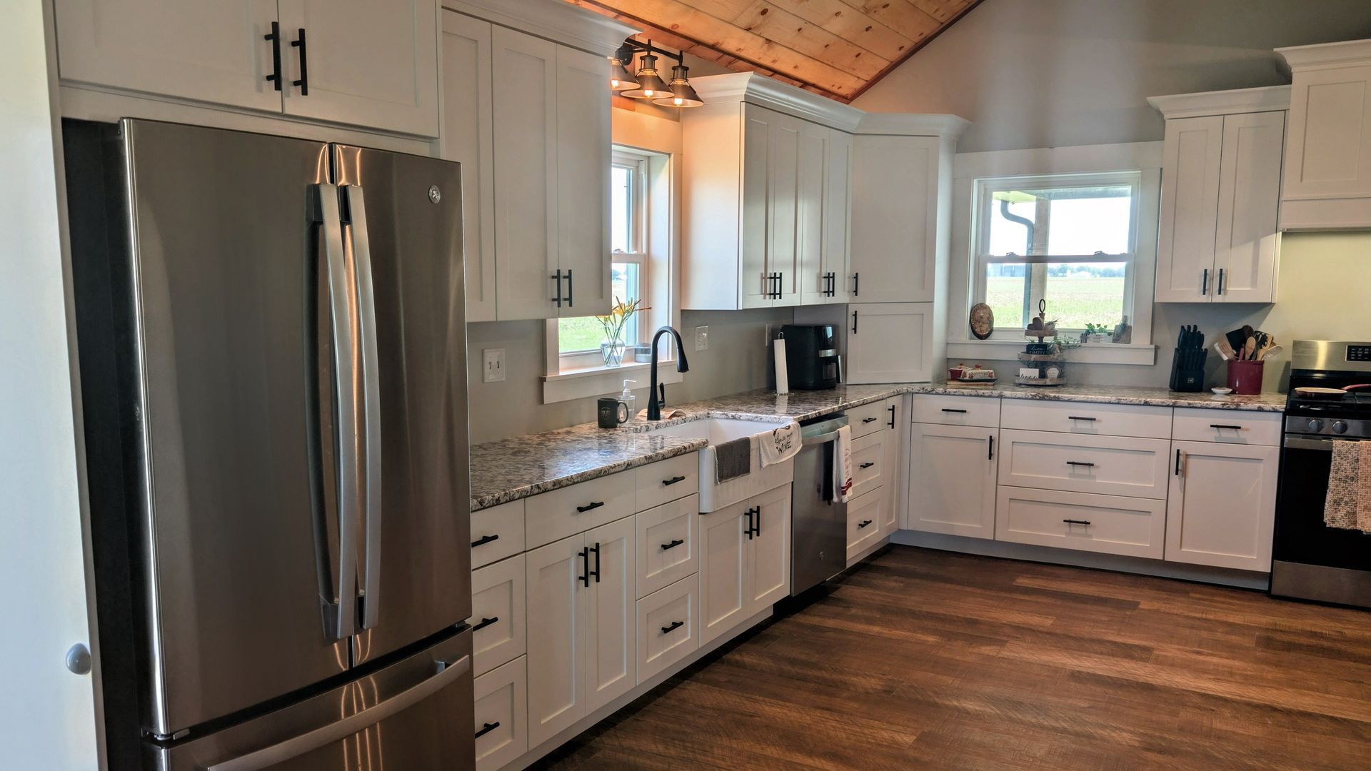 Custom white Sharker-style kitchen cabinetry with granite countertops, farmhouse sink, and black hardware in a Mid-Missouri home. Custom cabinets Columbia Missouri 