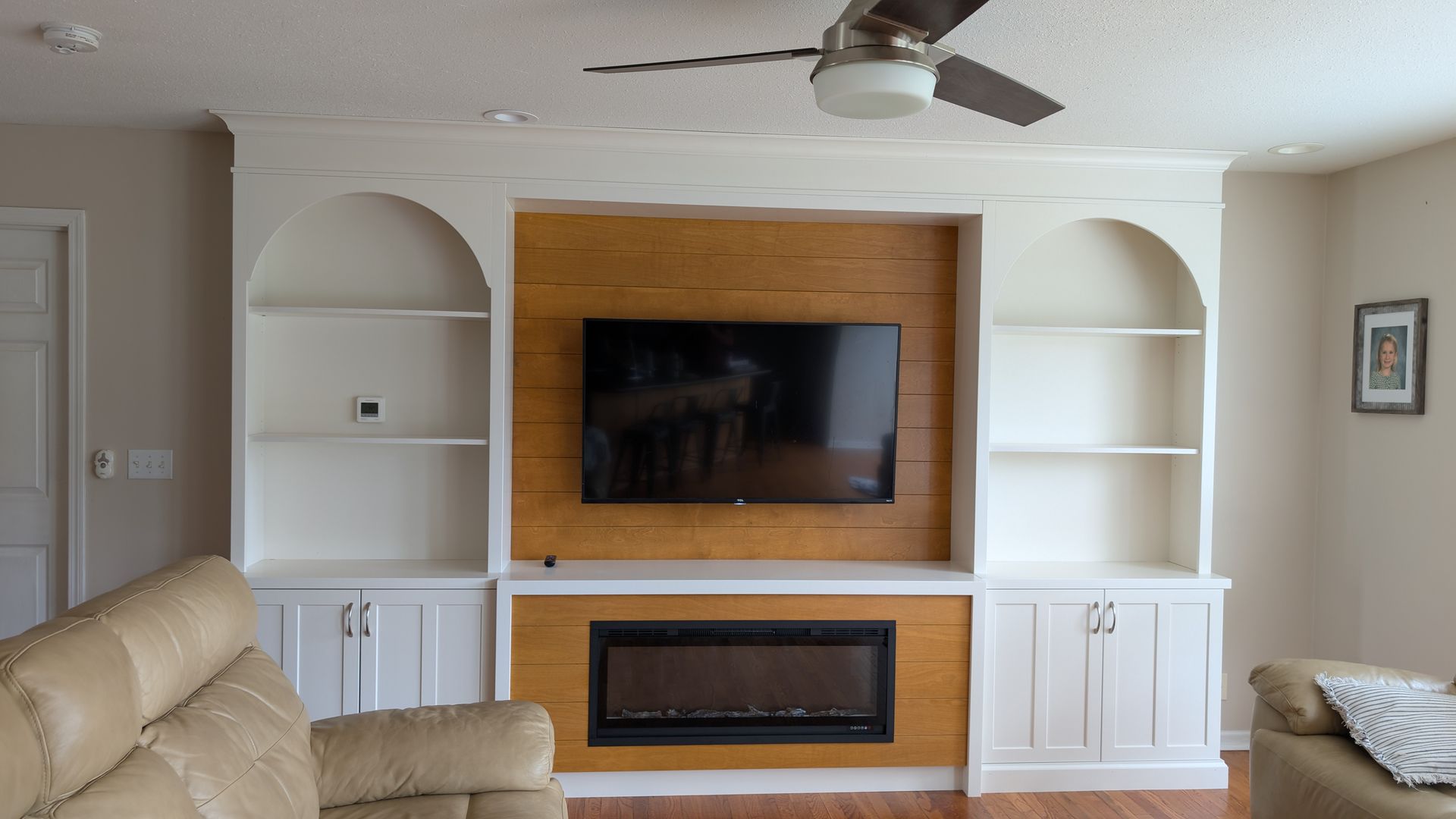 Custom white built-in entertainment center with arched shelving and natural wood shiplap accent wall in a mid- Missouri home