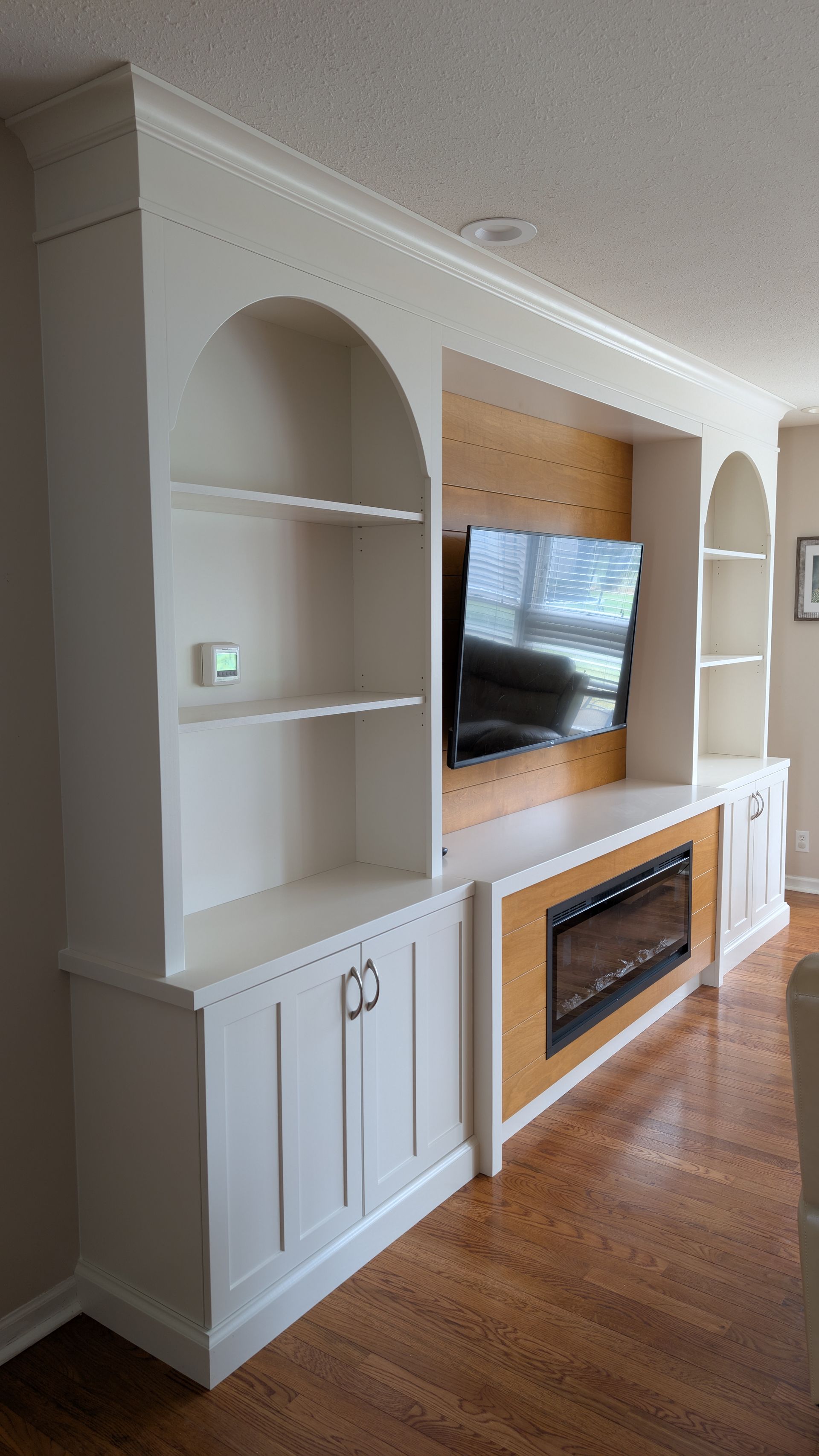 Custom white arched built-in shelving and entertainment center with natural wood shiplap accent wall in Columbia MO home. 