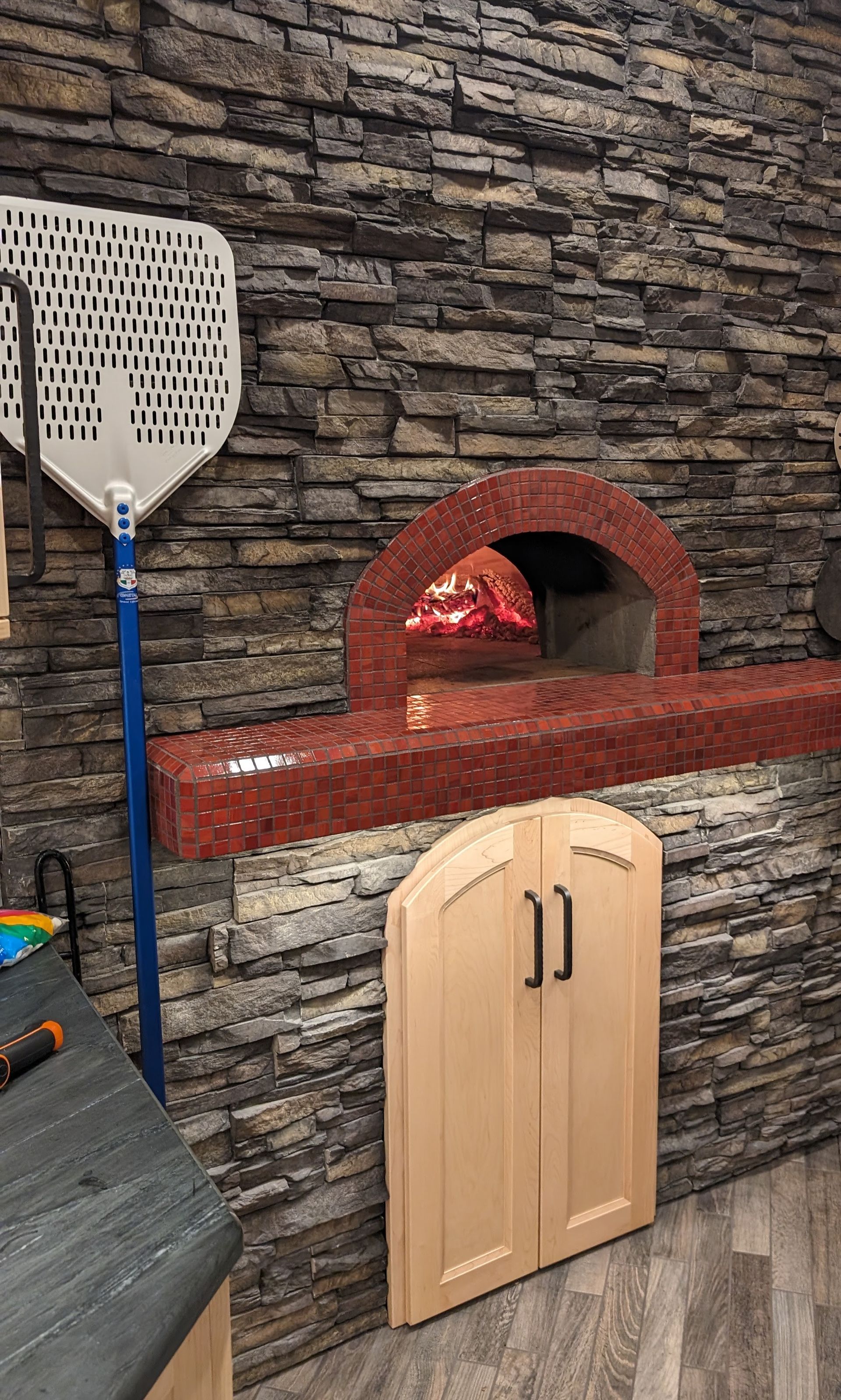 Custom arched wood cabinet doors integrated with a stone-clad pizza oven and brick hearth in an Ashland MO home. 
