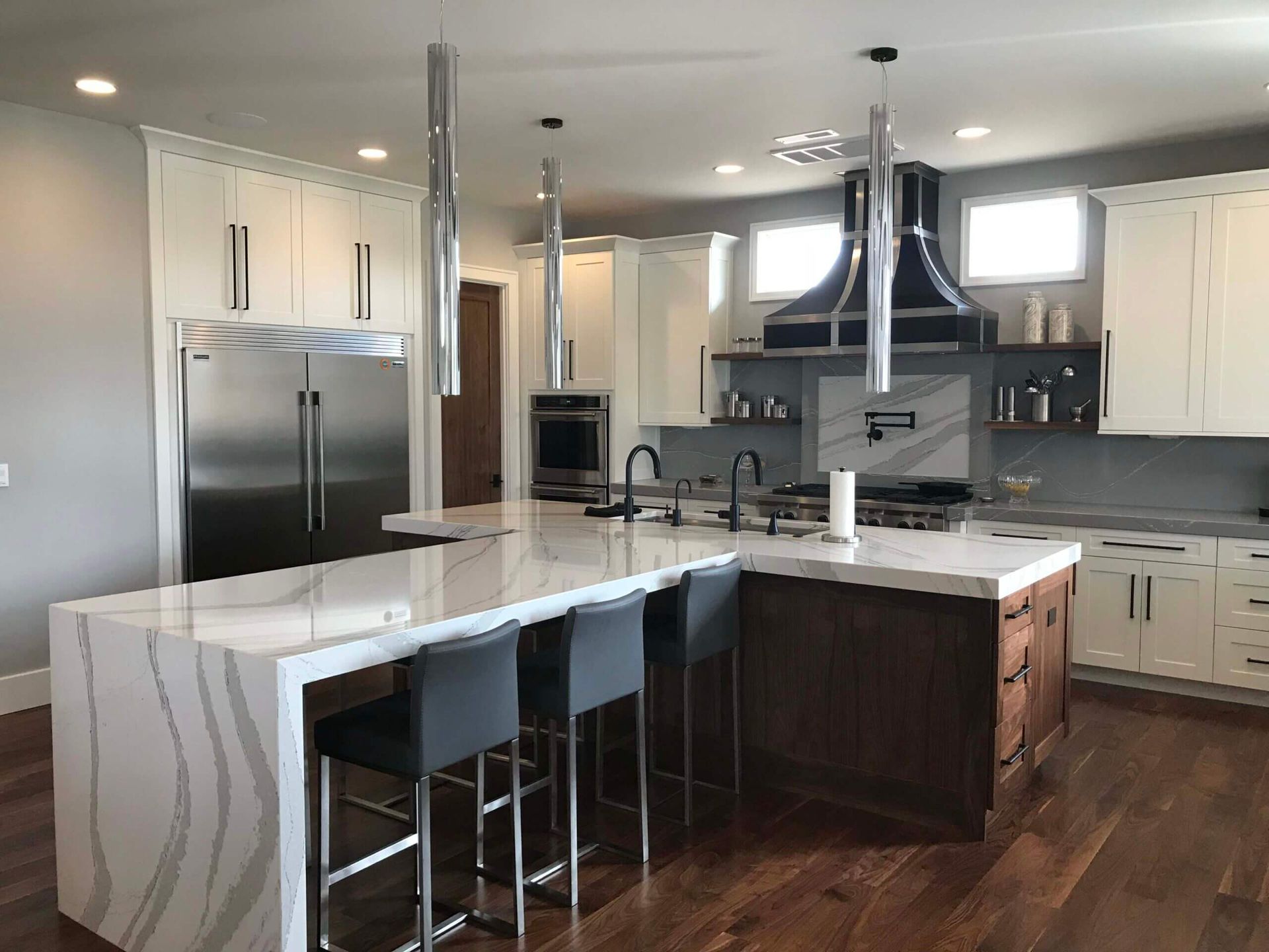 A kitchen with a large island , stainless steel appliances , white cabinets and hardwood floors. Custom cabinets Columbia Missouri 