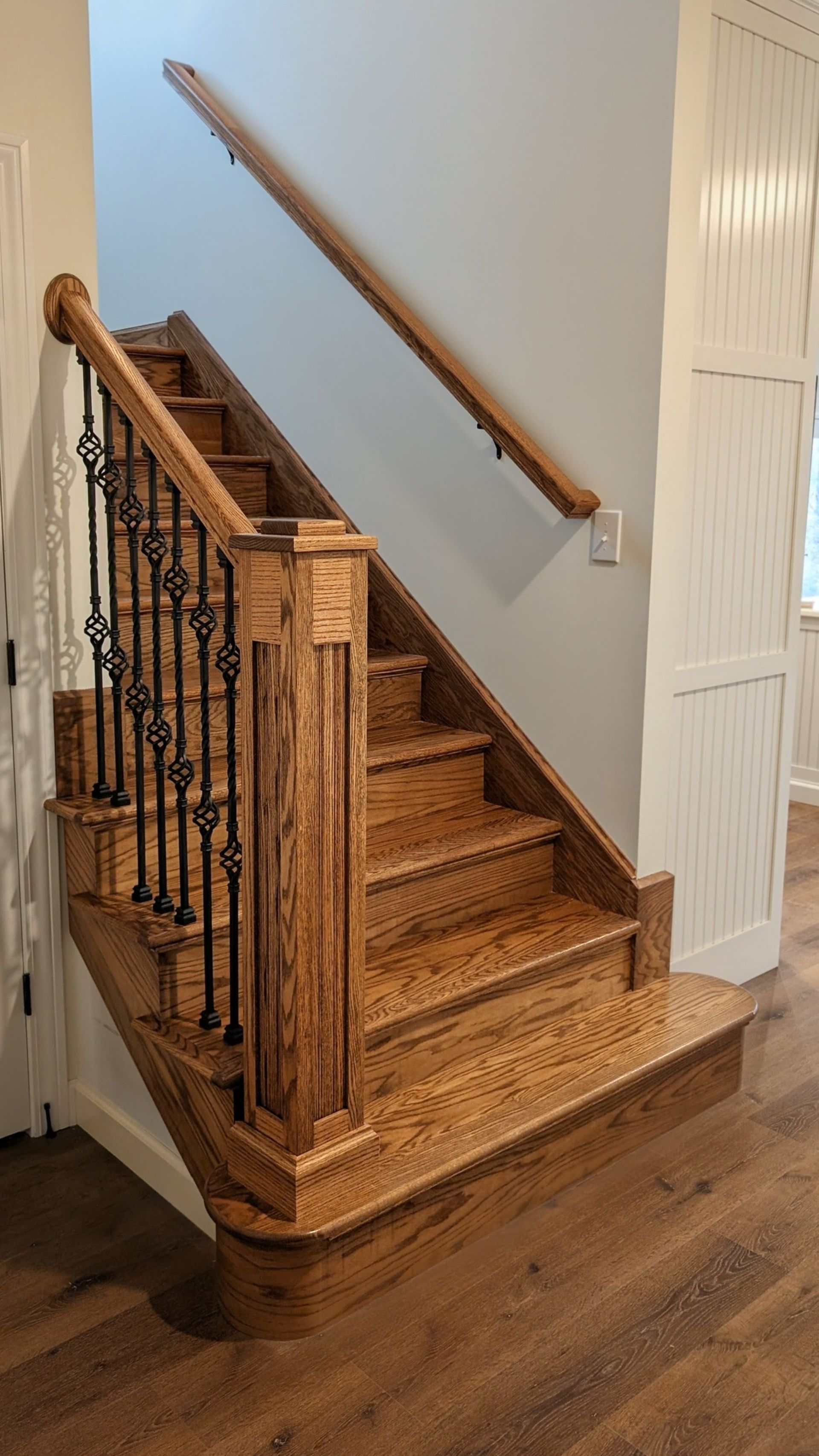 Custom oak wood staircase with decorative iron balusters and hand-crafted newel post in a mid-Missouri home. 
