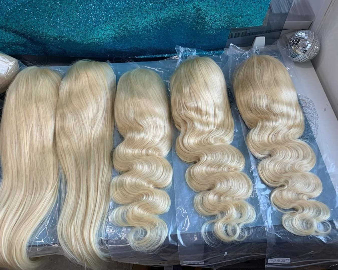 Five blonde wavy hair wigs displayed on a surface.