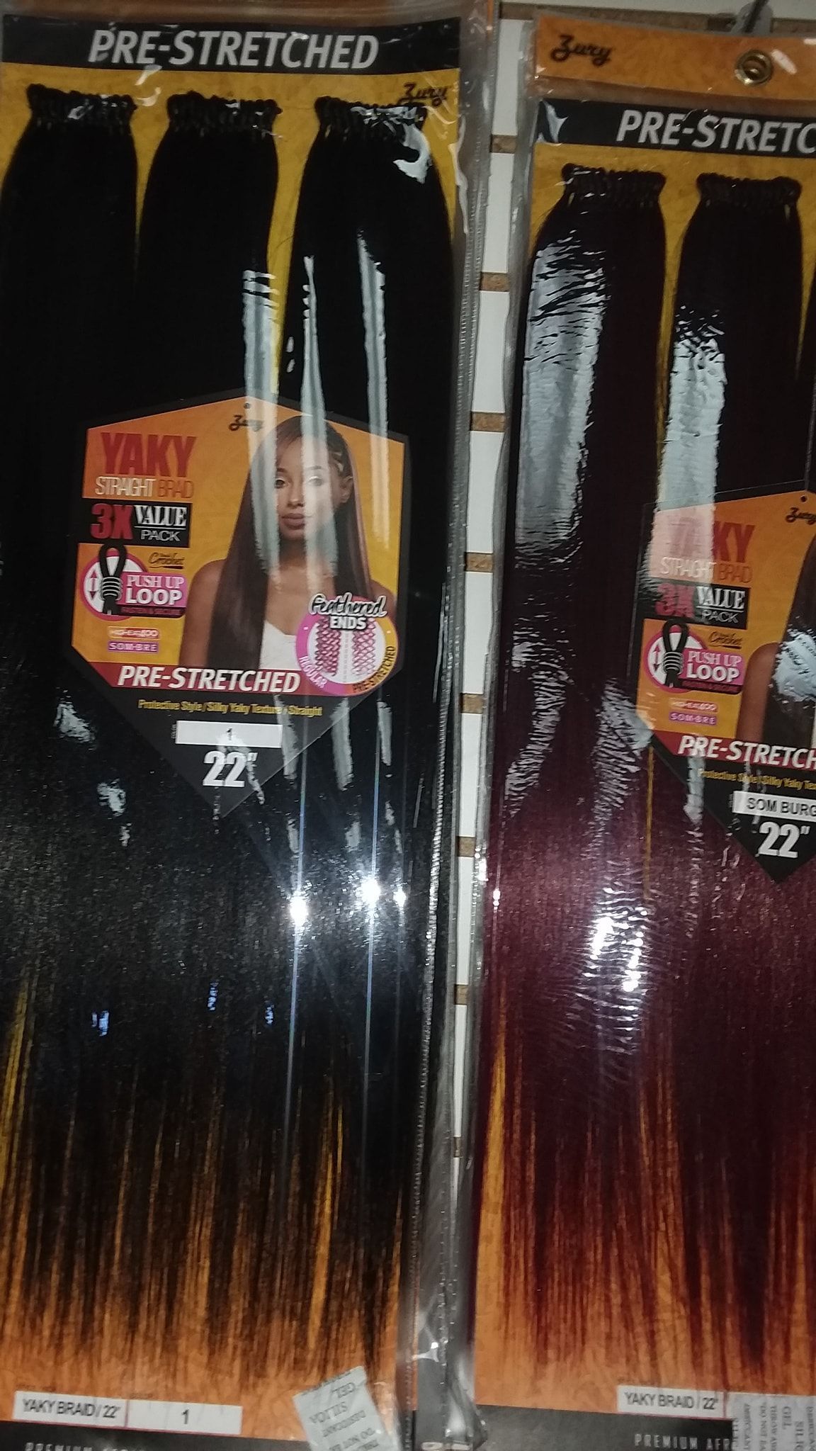 Two packages of pre-stretched braiding hair; one black, one burgundy. Each package shows a woman with long hair.