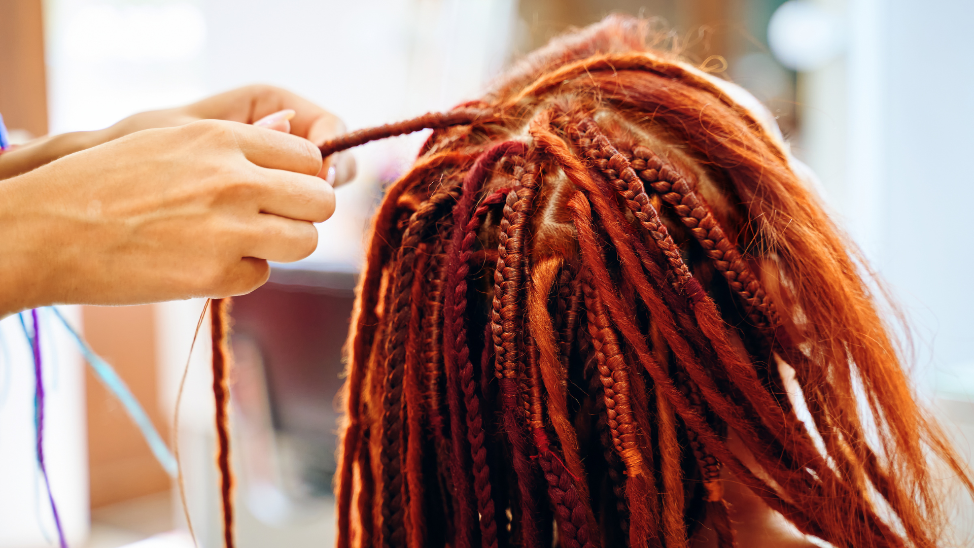 Hands braiding red dreadlocks.