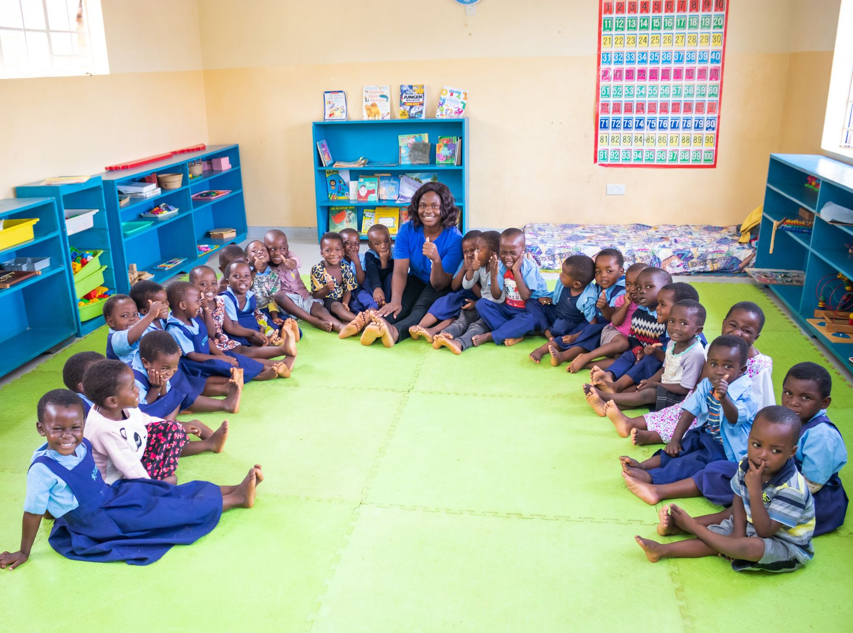 A teacher sits among children during a classroom session at The Sparkle Foundation, supporting young learners as they develop early skills and confidence in a safe learning environment designed to prepare them for the next stage of their education.