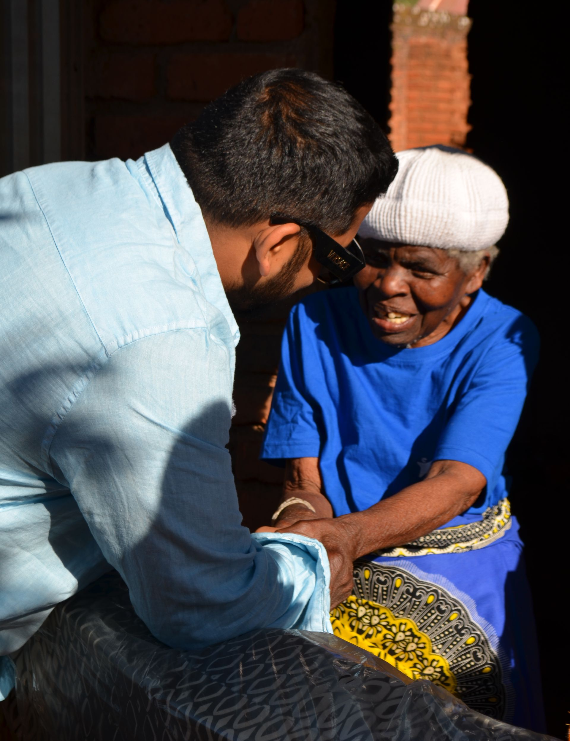 Zoheb Sayyed from Revo Realty holds hands with 86 year old Emily during his visit to her home in Malawi, where he helped provide a blanket, clothes, shoes and a mattress following the Revo Realty team’s charity trip with The Sparkle Foundation.