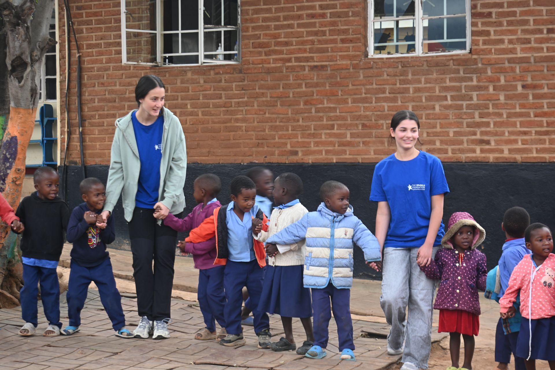 Luce, a volunteer with The Sparkle Foundation, joins children during their morning circle in Malawi, taking part in the group activity and sharing a playful moment with the children.