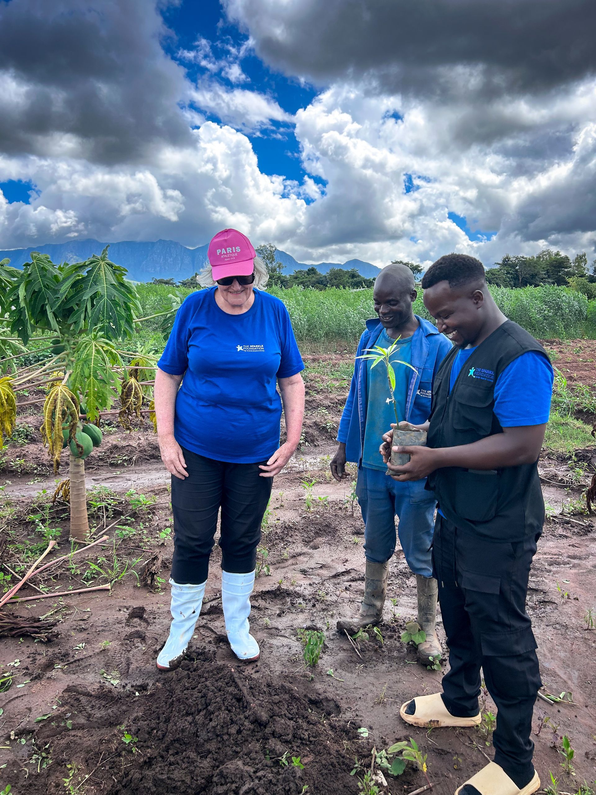 Leith stands at the Sparkle Farm as she prepares to plant a tree, contributing to long-term agricultural production that supports food provision for children in the community.