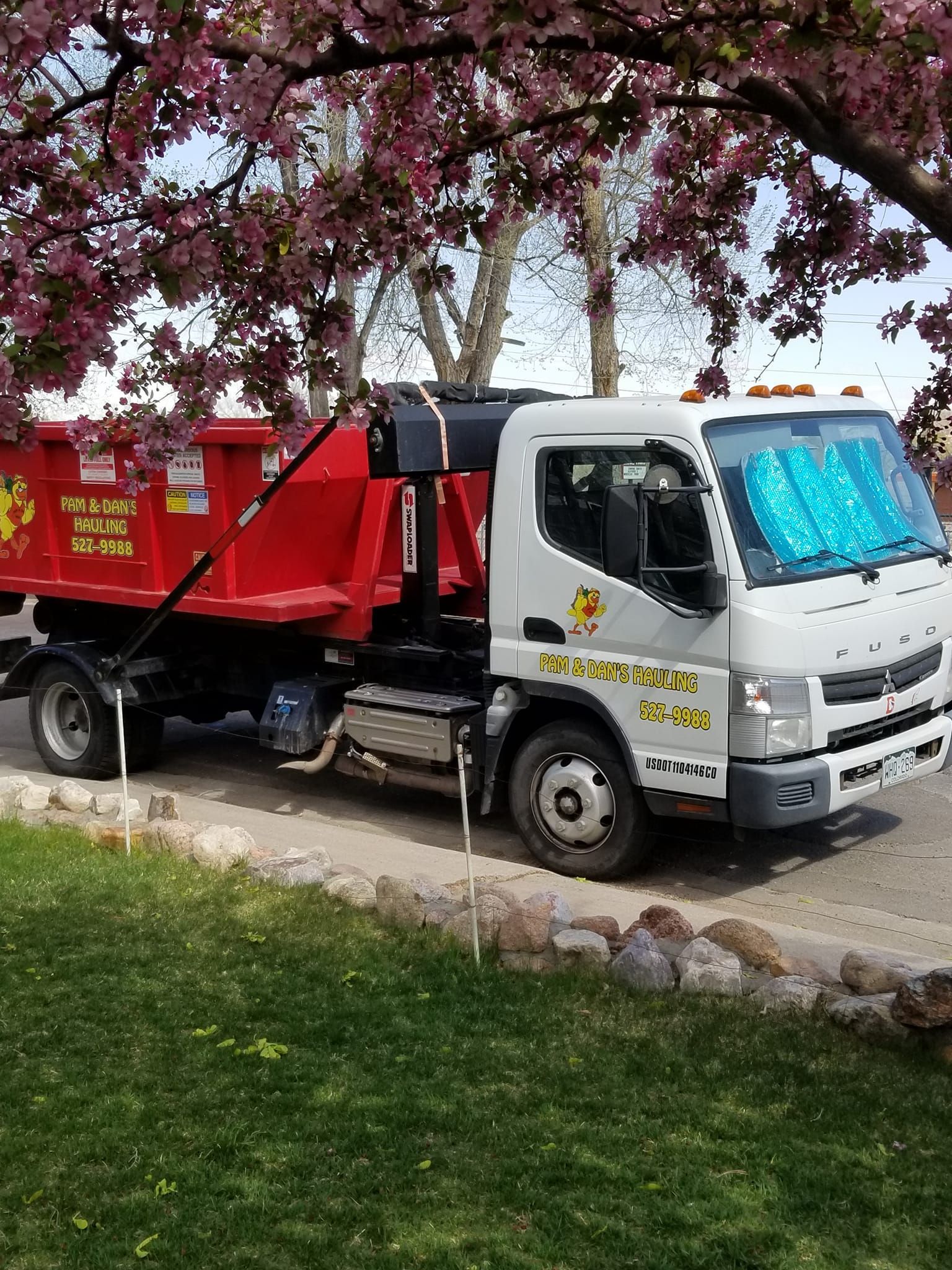 A dump truck is parked in front of a cherry blossom tree.