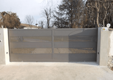 Un grande cancello metallico è aperto su un vialetto davanti a una casa.