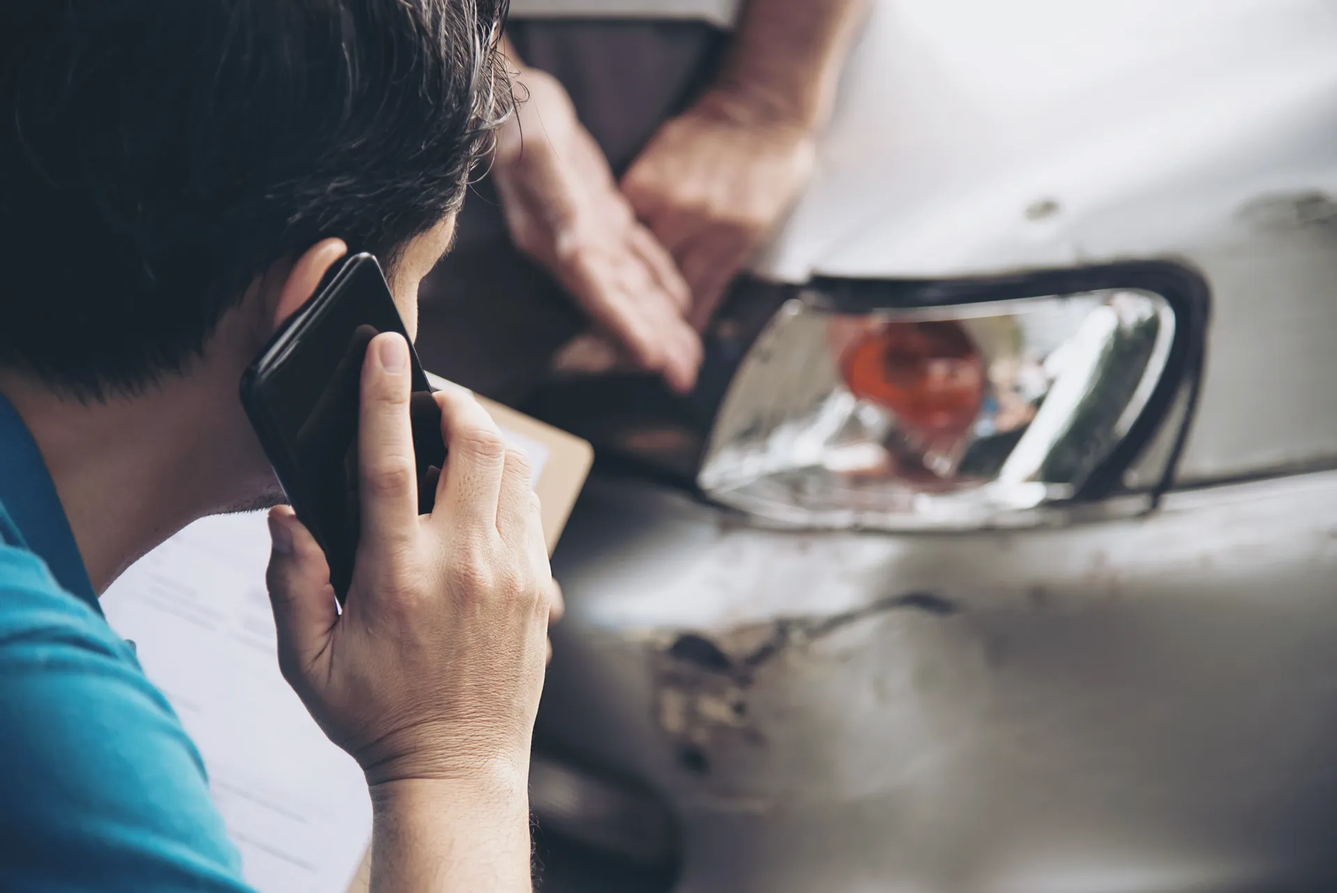 Person on a phone watches a video call on a car mirror while another person stands nearby.